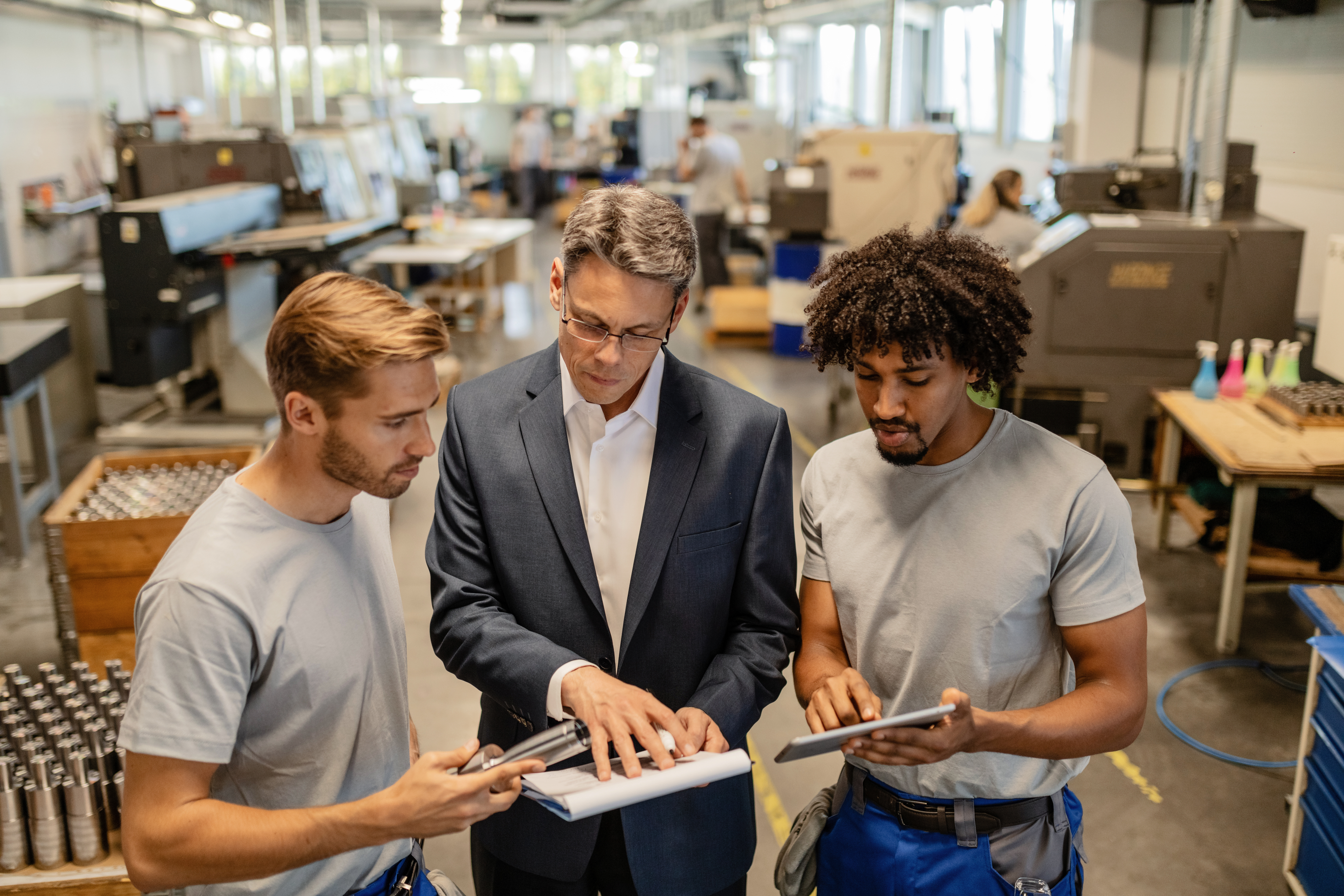 Team discussing plans over a tablet in a factory setting.